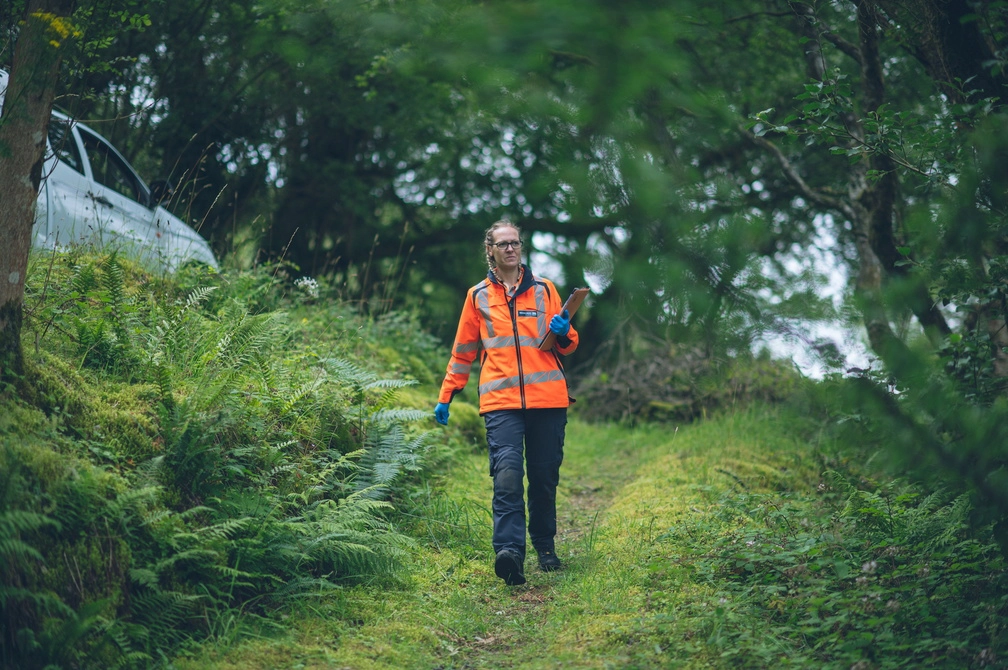 Employee in high vis walking through nature in hi vis and holding a clipboard